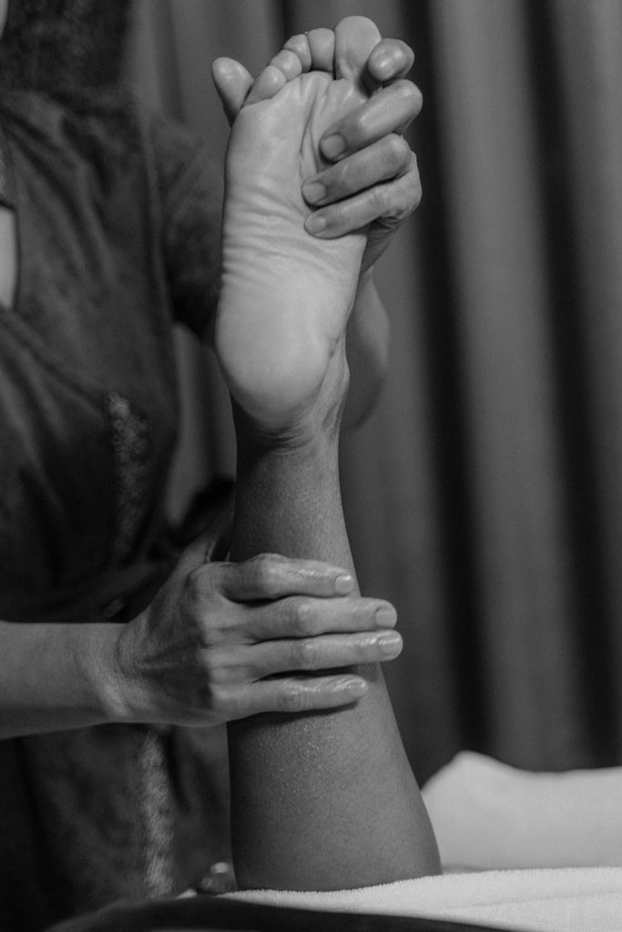 A black-and-white image of a massage therapist performing an ankle and foot massage.