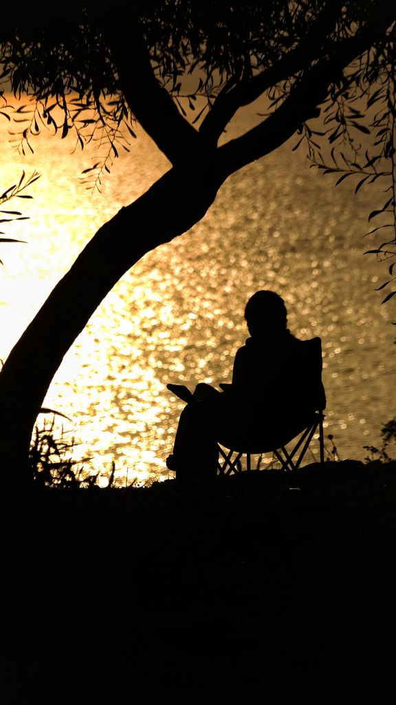 A serene silhouette of a person sitting by a lake during sunset, creating a peaceful scene.